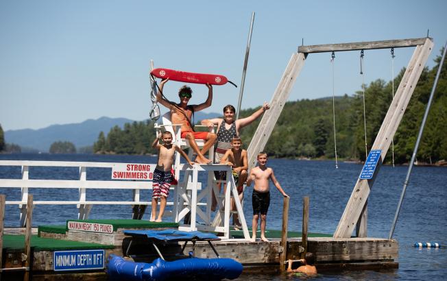 A lifeguard holds up a life vest while taking a picture with kids on a dock.
