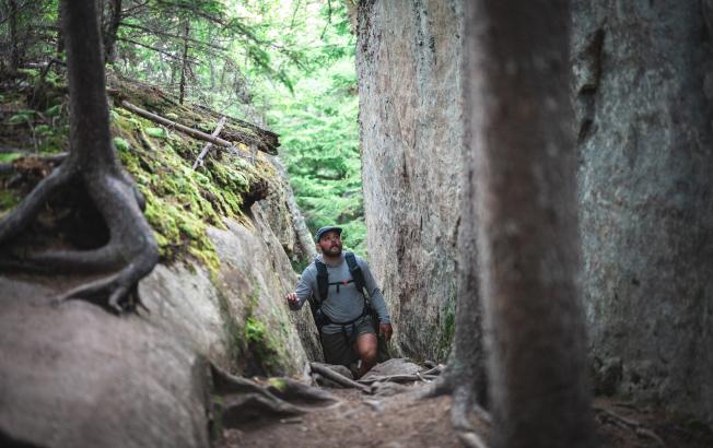 A man hikes between two rock slabs in the woods.