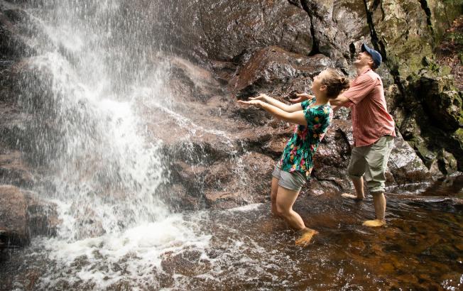 Two young people stand beneath a waterfall.