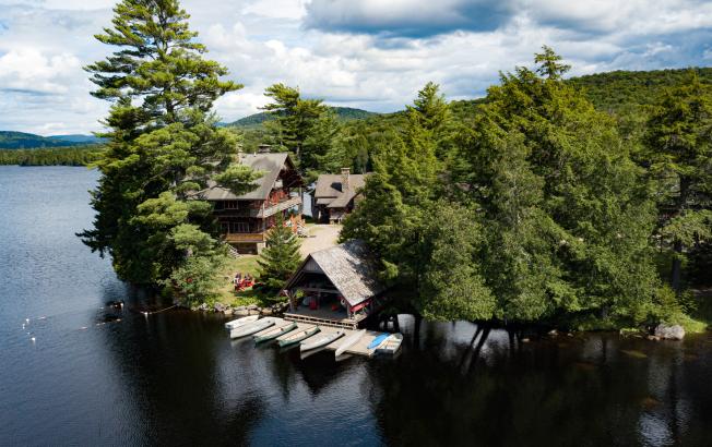 A grand lodge with a boat house sitting on the edge of a lake in summer.