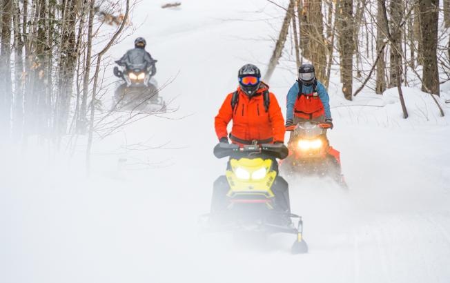 Three snowmobilers ride on a winter trail.