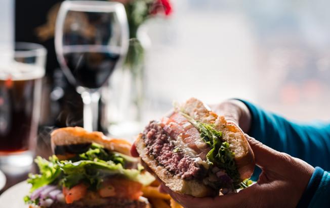 A woman holds a burger over a plate.