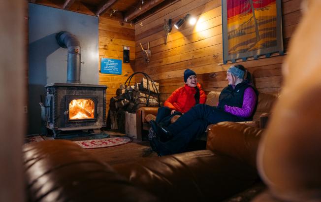 Two women sit and laugh in a cabin.