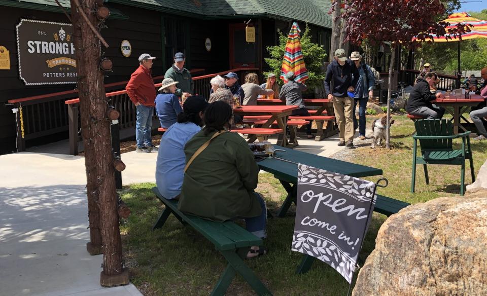 A phot taken outside of the strong rope taproom building with several people sitting at picnic tables outside on a sunny day