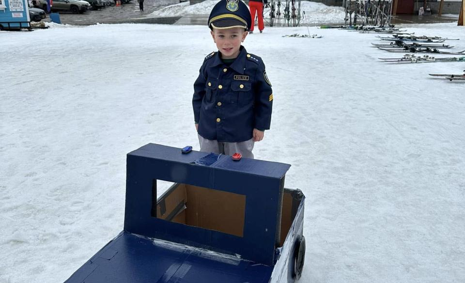 a little boy dressed as a cop standing behind his cop car sled