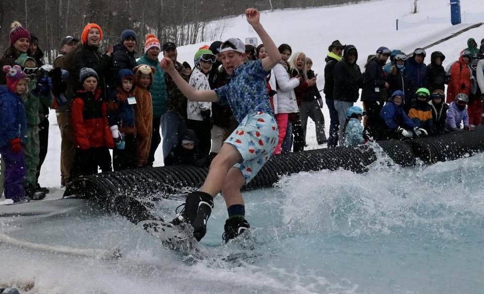 a man skimming across the water on a snowboard dressed in beach clothes