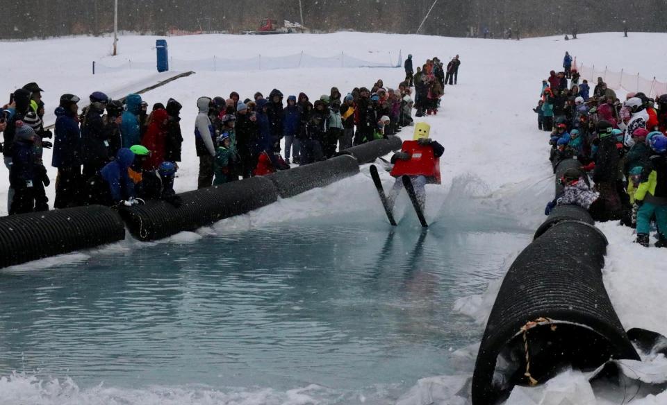 a person dressed as a LEGO mas just hitting the waters edge after skiing down the hill