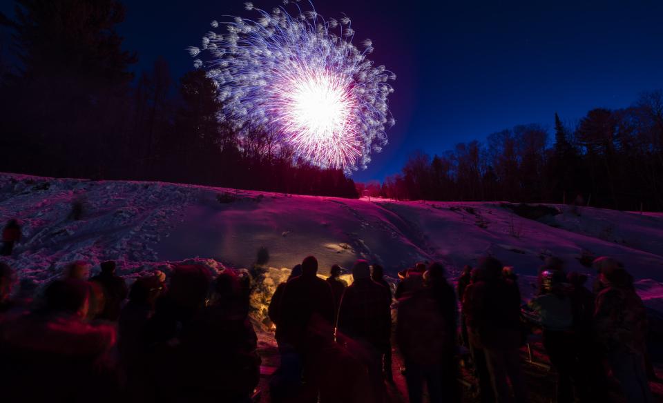 fireworks above a group of people around a bon fire