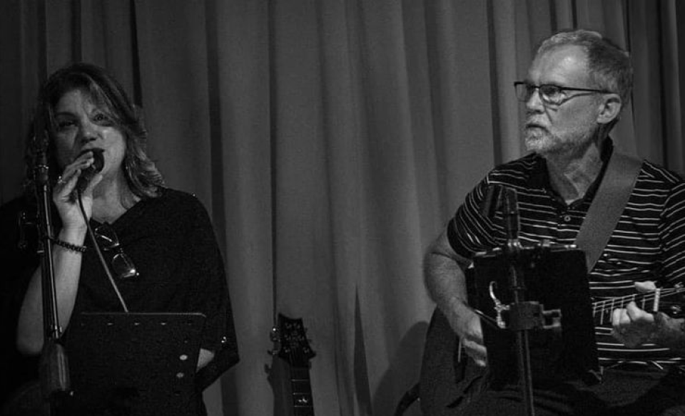 A woman singing and a man sitting next to her playing the guitar