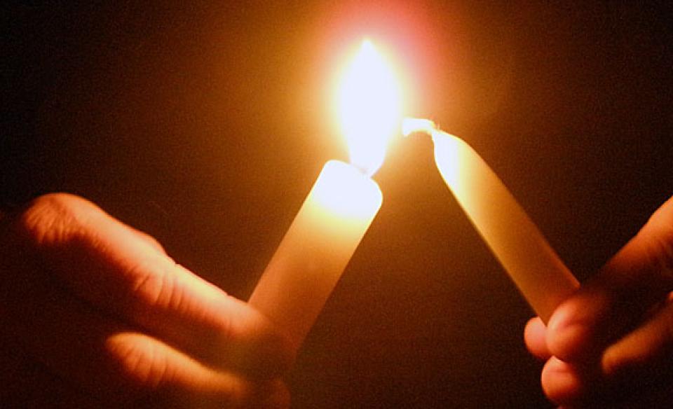 a close-up photo of two people lighting their small candles together