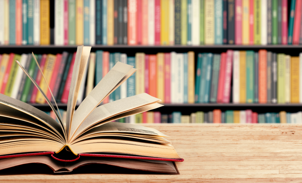 A couple of books open and on a table with library books on shelves in the background