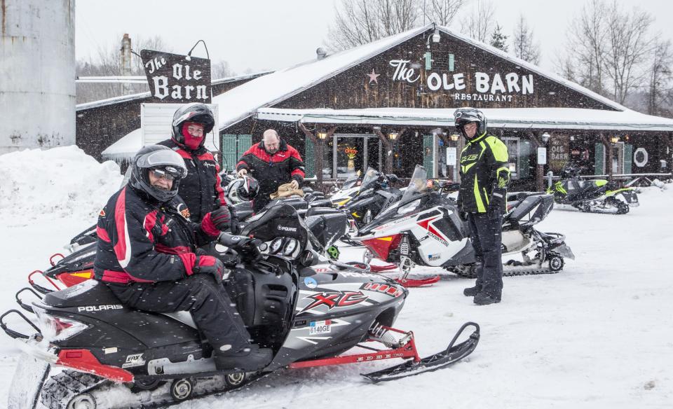 Five colorful snowmobiles line up on a snow-covered field with misty mountains in the background