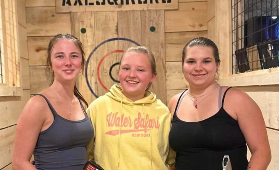 three girls posing with their axes in front of the bullseye
