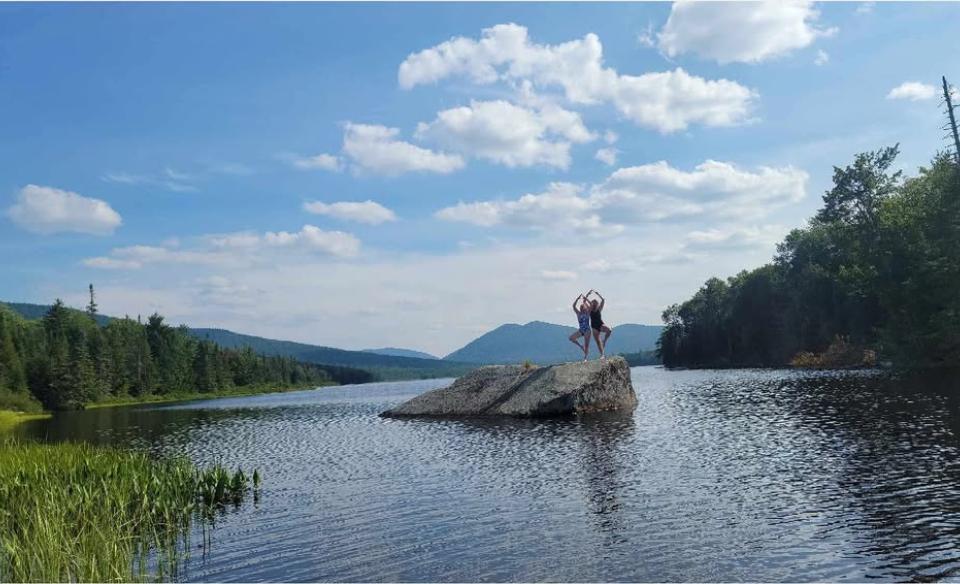 Two people doing a standing yoga pose on a large boulder in the lake
