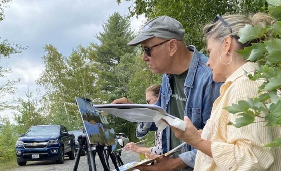 Three people standing at their easles painting the natural scene before them