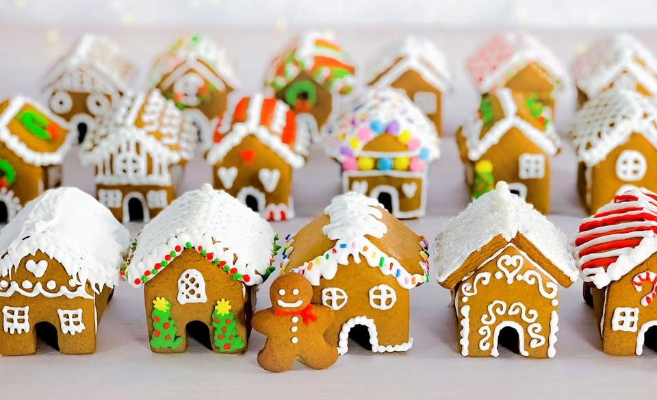 A gingerbread man cookie standing in front of three rows of mini gingerbread houses all nicely decorated