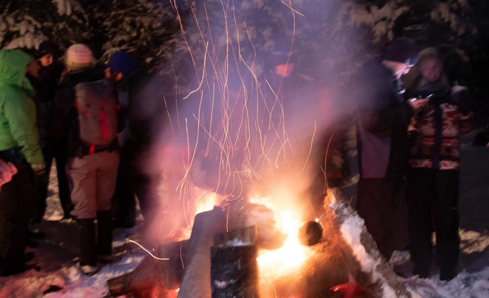 a photo of an outdoors fire at night with people standing in the background