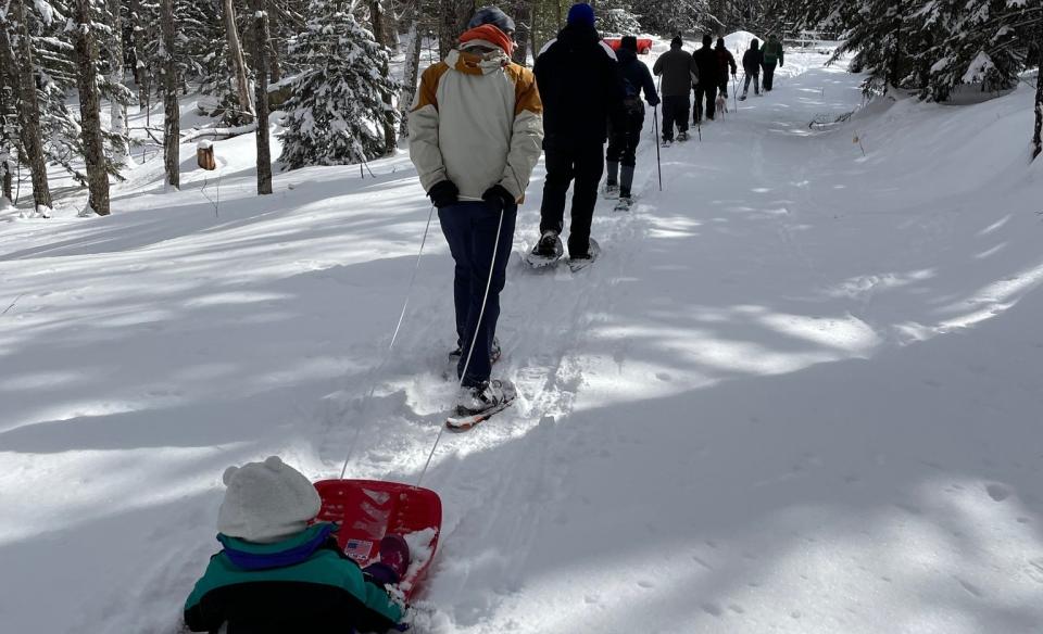 a line of people on a guided tour with a lady pulling her child in a sled