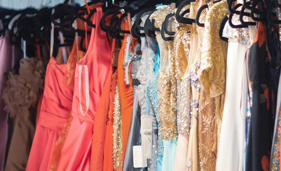 A line of prom and formal dresses hanging on a rack
