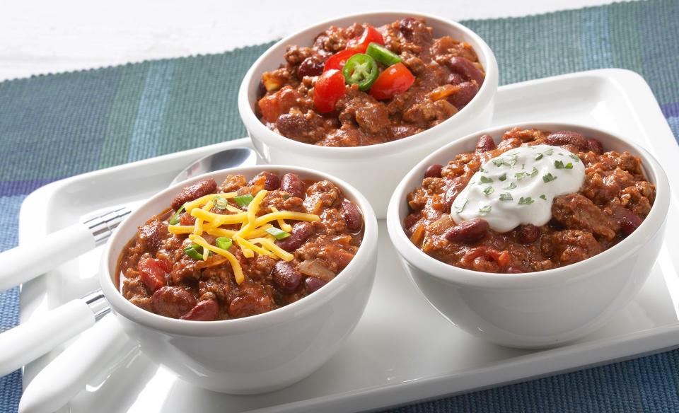 Three small white bowls each with chilli in it with different toppings to garnish each