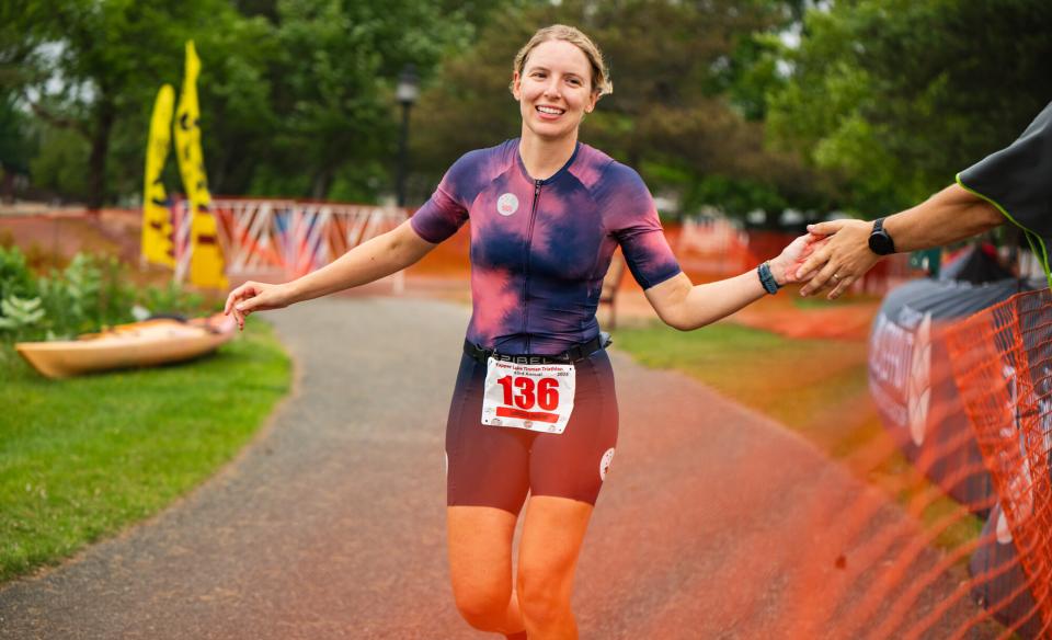 A smiling triathlete reaches out for a high-five while running toward the finish line of the Tupper Lake Tinman Triathlon.