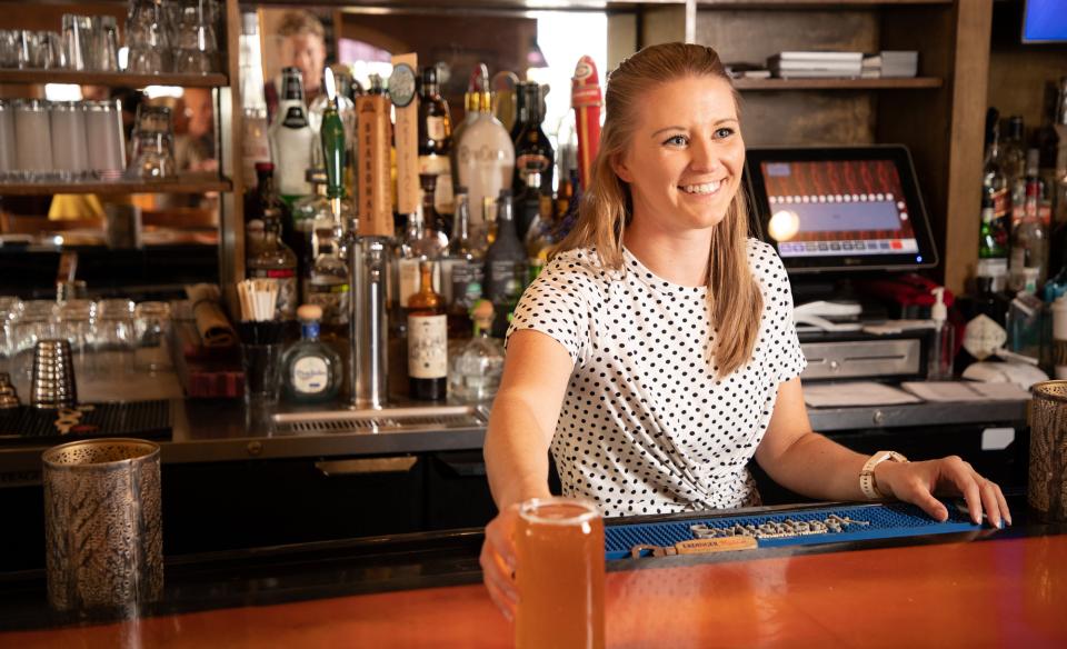 A woman behind the bar serves a beverage and smiles