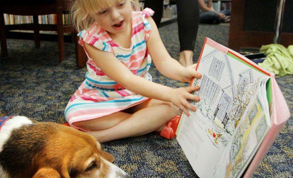 A little girl reading a story to a beagle who is laying on the floor next to her
