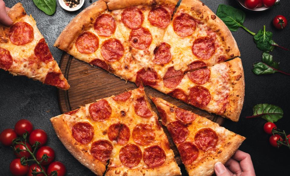 a pizza with people taking away a couple slices