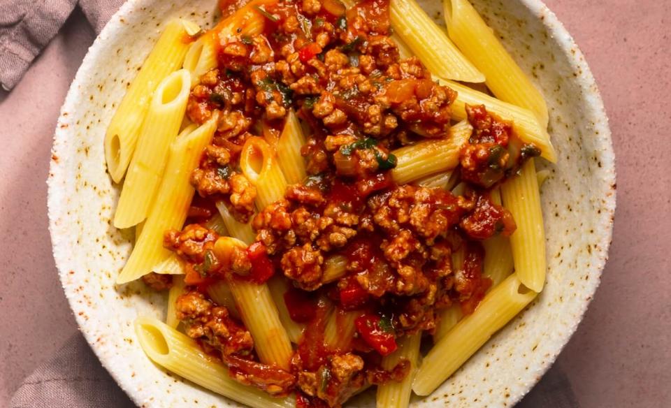 a pasta plate full of penne pasta with a red meat sauce on top