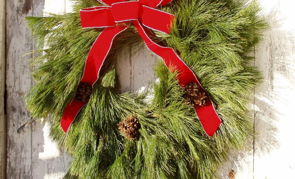 Photo of a hand made wreath using pine branches with a red bow tied to the top