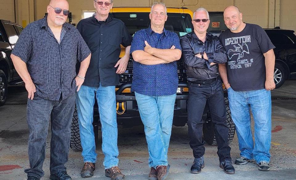 5 men lean against a yellow vehicle in a garage