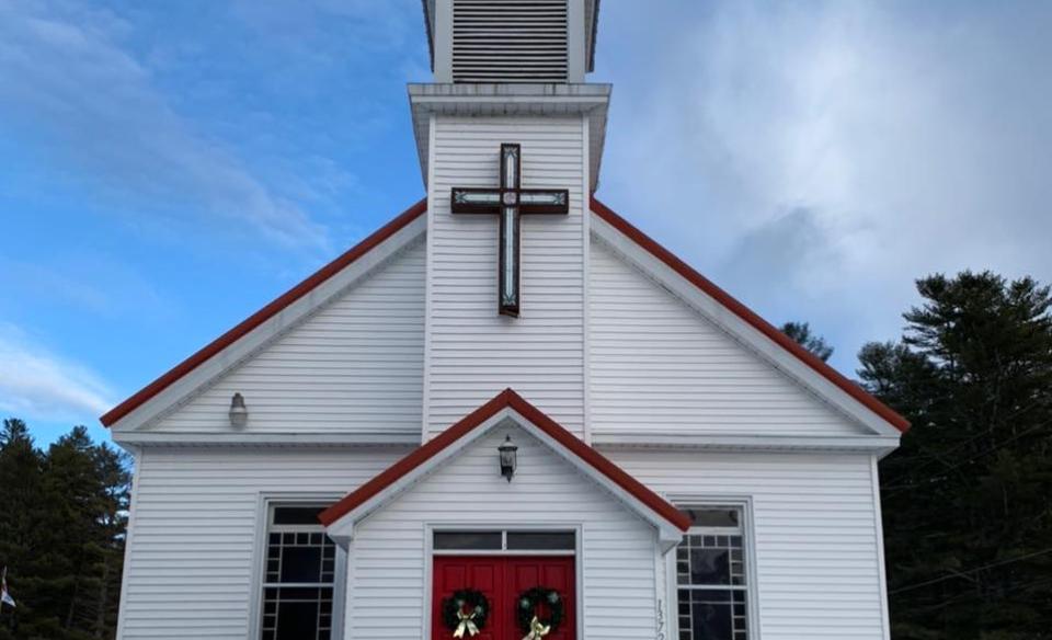 Wells Methodist Church with a red roof and a large cross on the front.  Two red doors are decorated with evergreen wreaths.