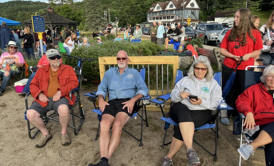 Four people sit in lawn chairs in front of a wooden fence