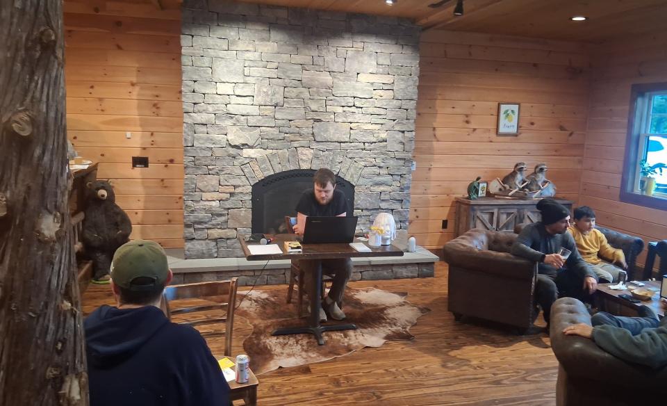 A person works on a laptop at a table in a rustic lodge-style room with a stone fireplace