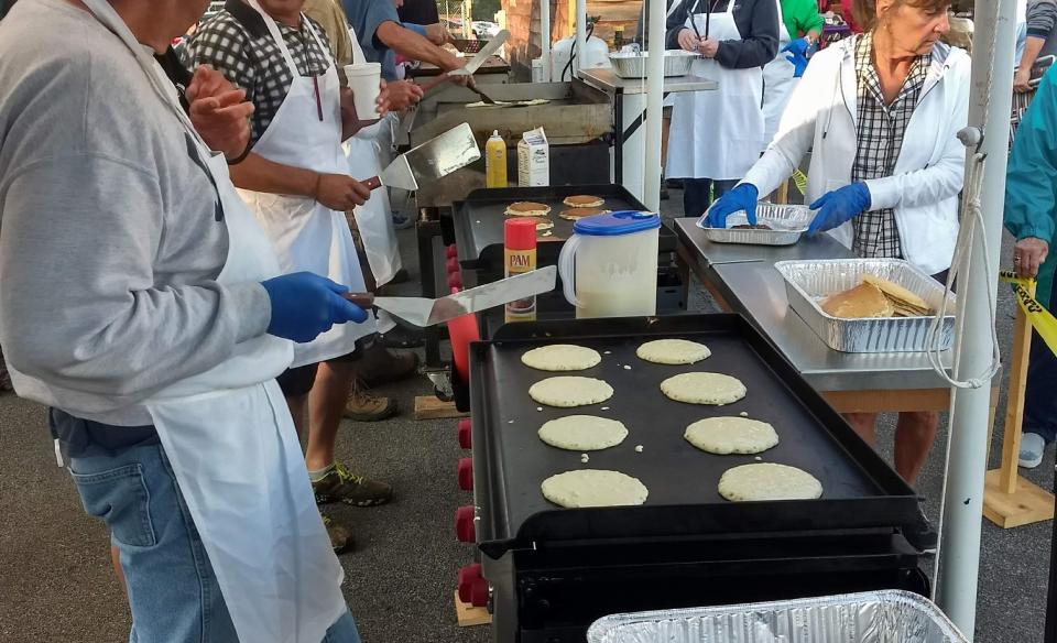 A group of volunteers cook and serve pancakes at an outdoor event.