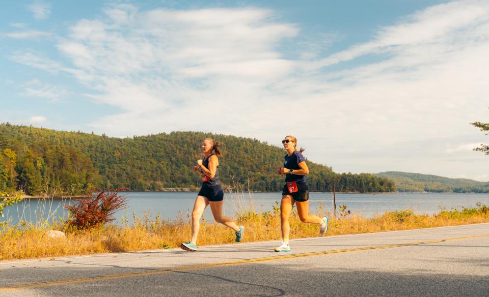 Two women run along a paved road during the Adirondack Marathon.