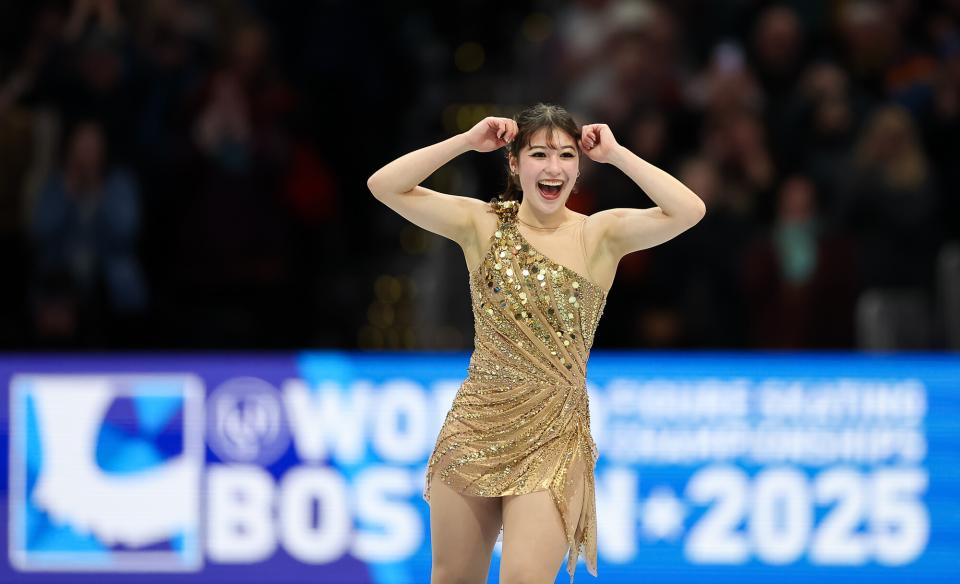 Male figure skater in brown long sleeve and long pant spandex suit performs a crouched move on ice