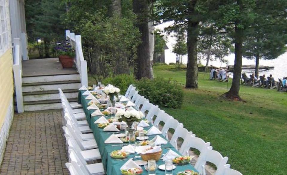 An event table set up outside on the lawn and covered with green cloth and white flower arrangements.