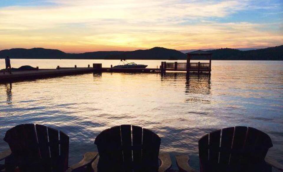 Adirondack chairs lining the beach by the water at sunrise.
