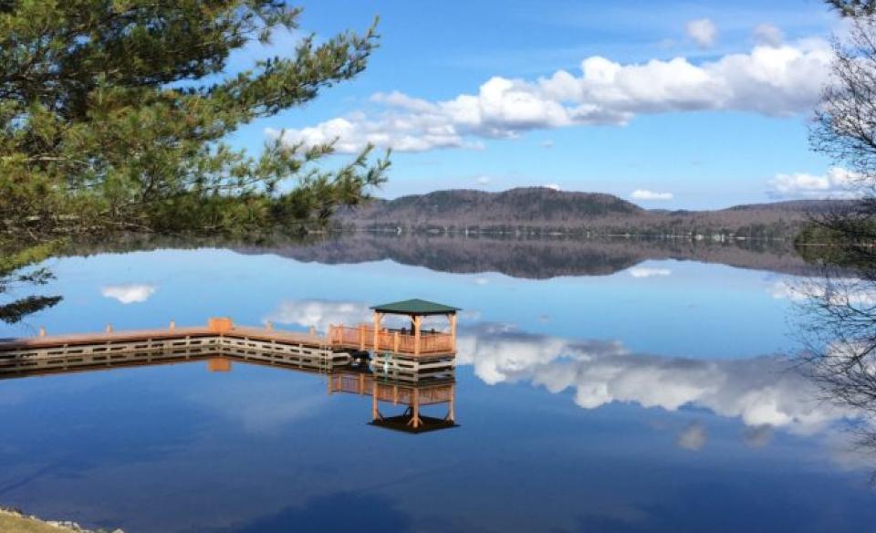 The gazebo on the dock from above on a perfectly still day where the lake reflects the clouds and mountains.