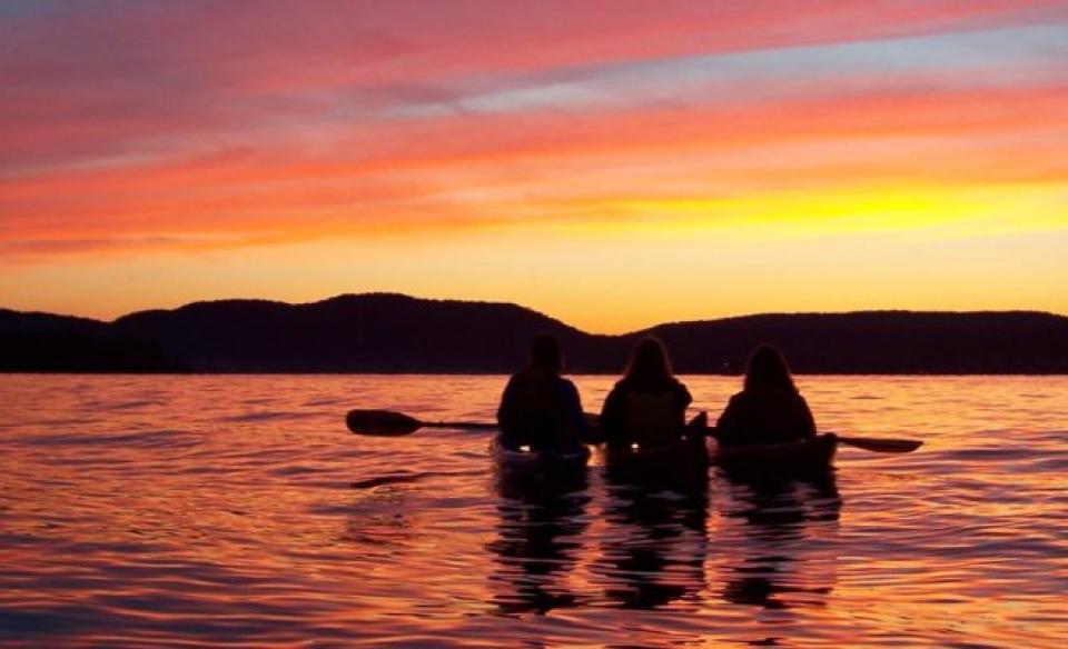 Three kayakers on the water enjoying the sunset over the mountains.