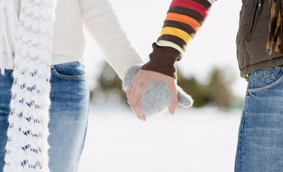 Two people holding gloved hands and walking in the snow