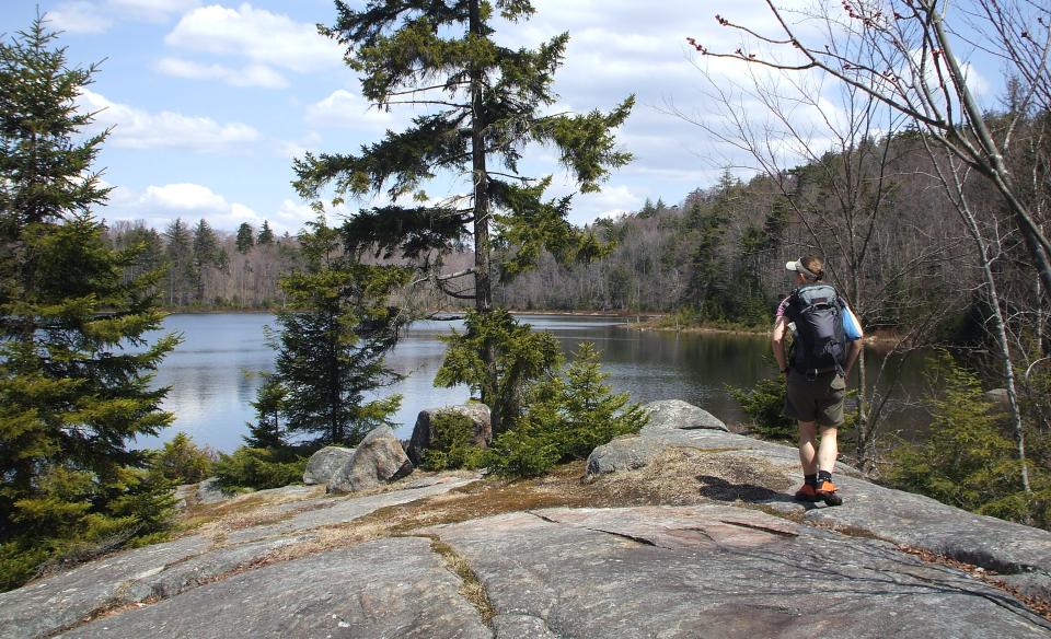 A woman walks towards a pond on an exposed granite trail.