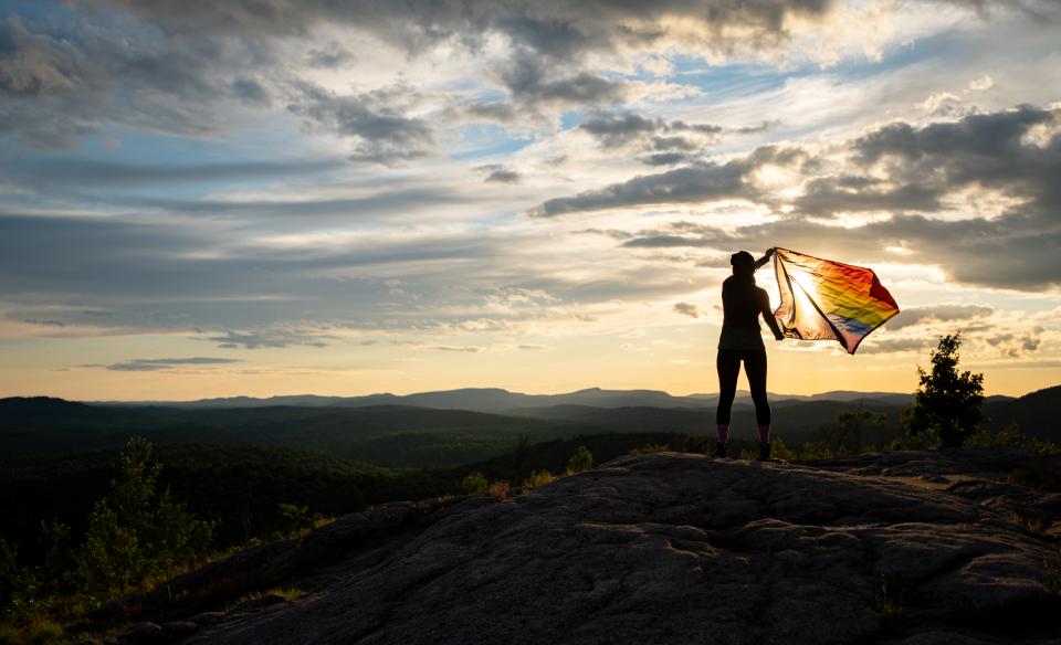 A hiker flying a pride flag on the summit of a mountain.
