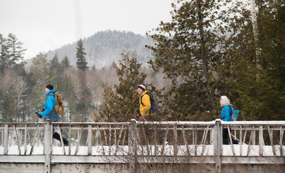 Three people snowshoeing across a bridge at the AIC