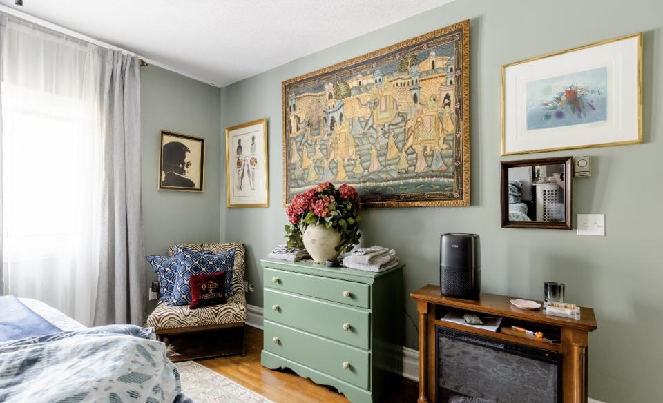 A guest bedroom with electric fireplace and wingback chair.